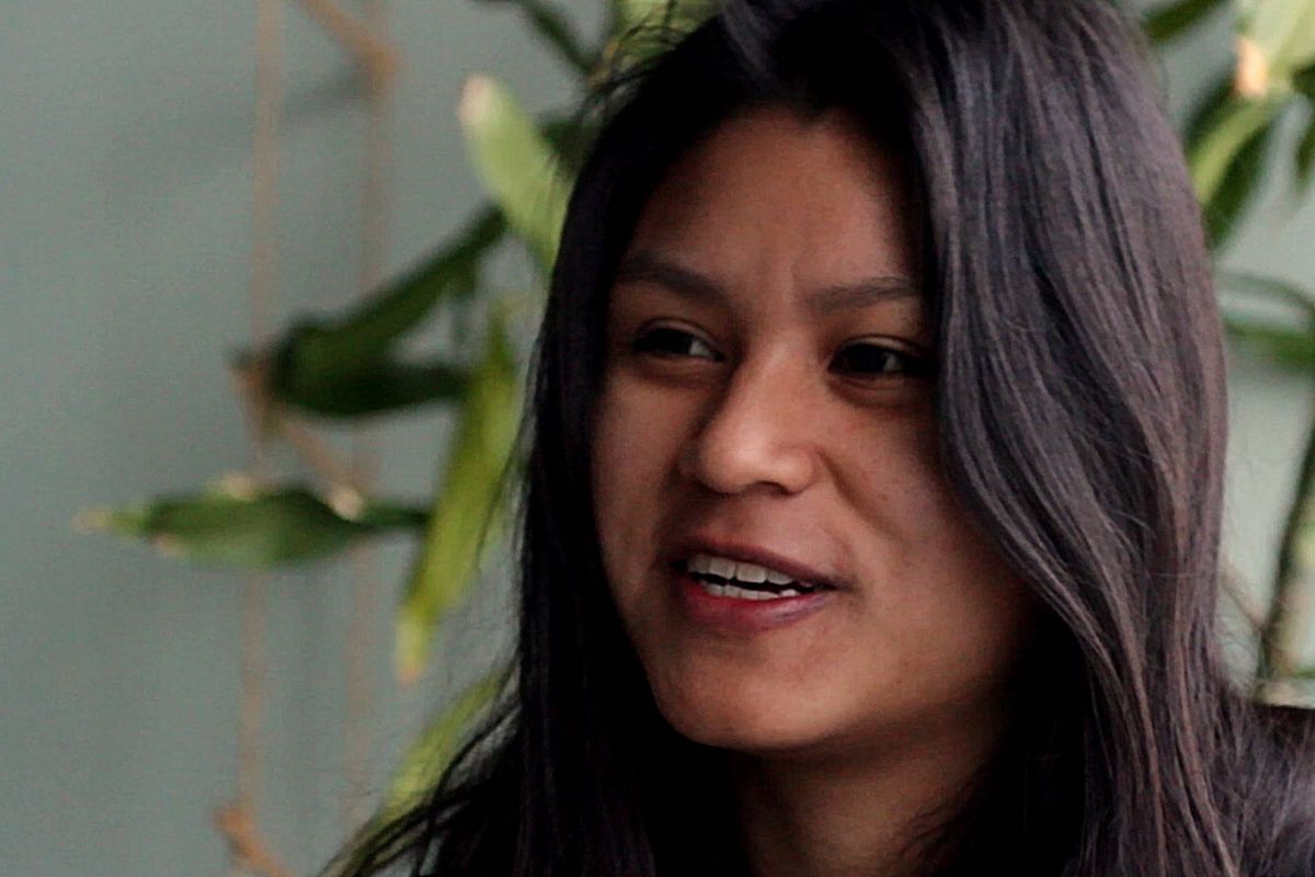 Portrait of a smiling young woman, a plant on the background.