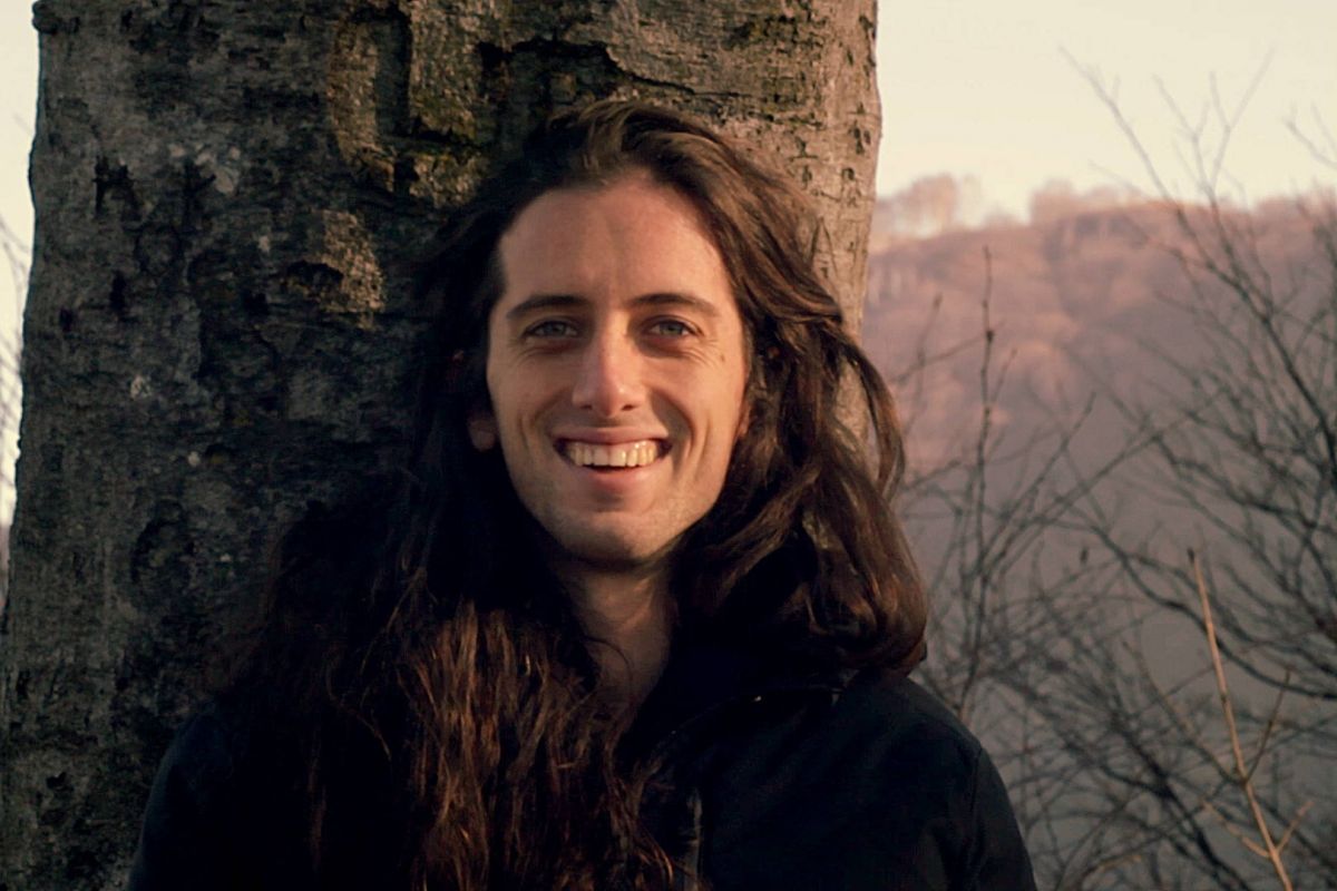 Portrait of a smiling young man, trees and mountains on the background.