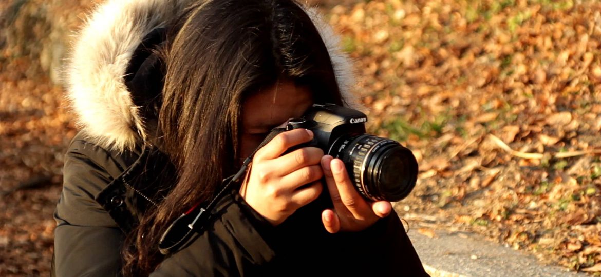 Girl filming with a camera in the woods.
