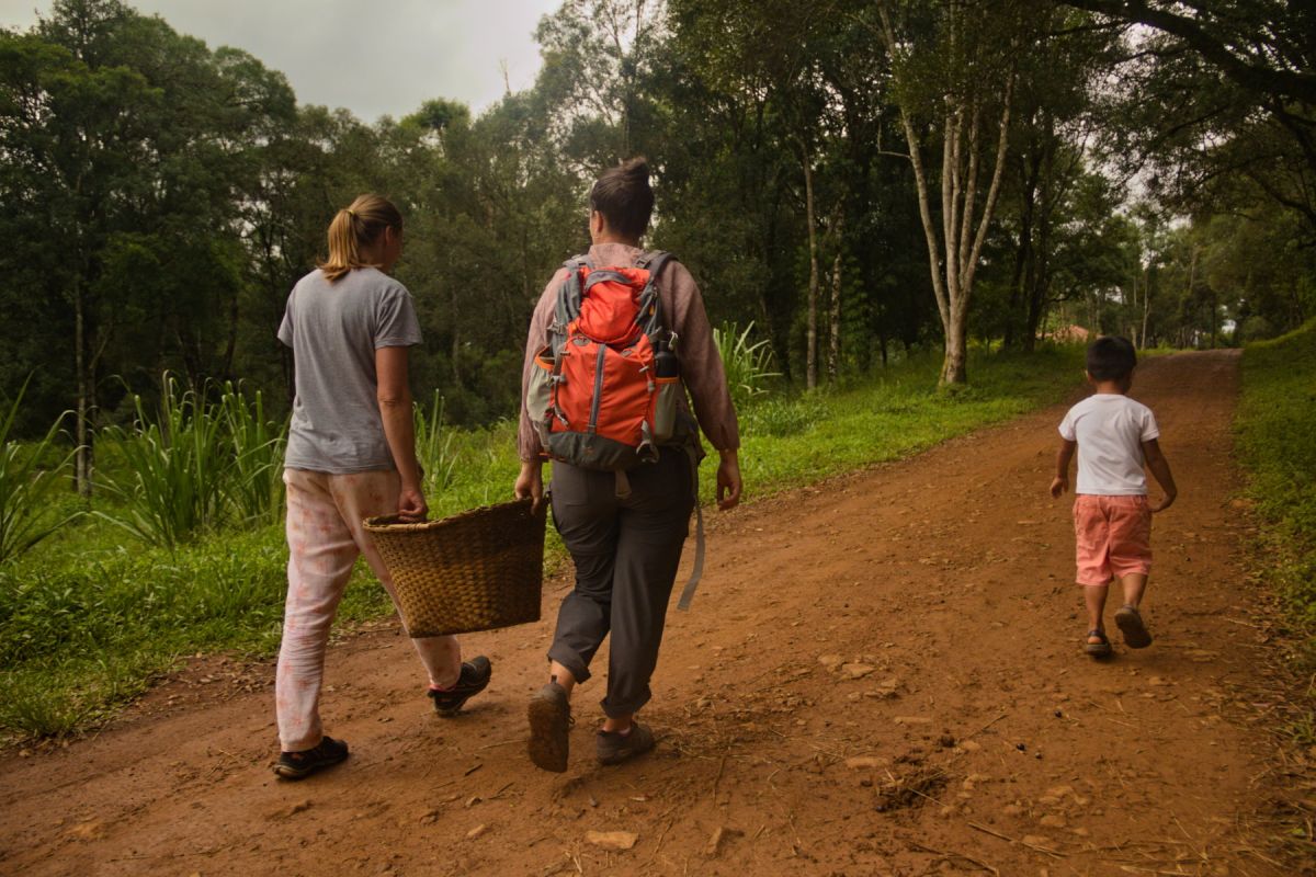 Two women bringing a basket full of corn, and a kid walking besides them.